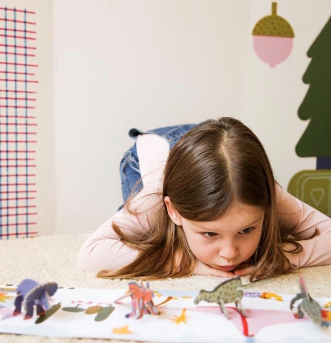 A girl playing with her dinosaur puzzle toys and play mat