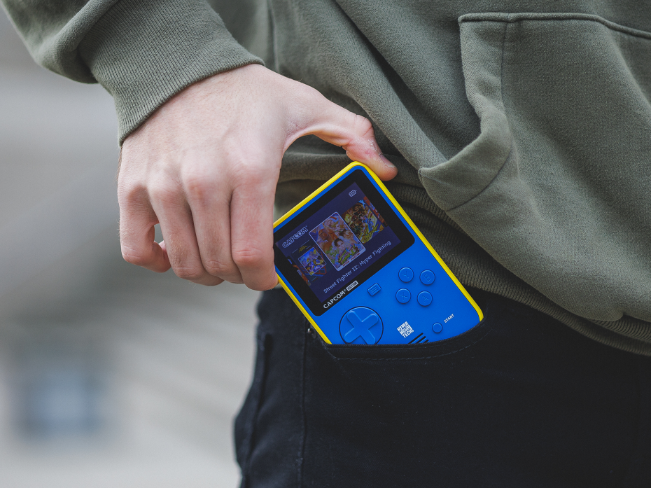 The Super Pocket Capcom Edition, front facing, being put into a trouser pocket.